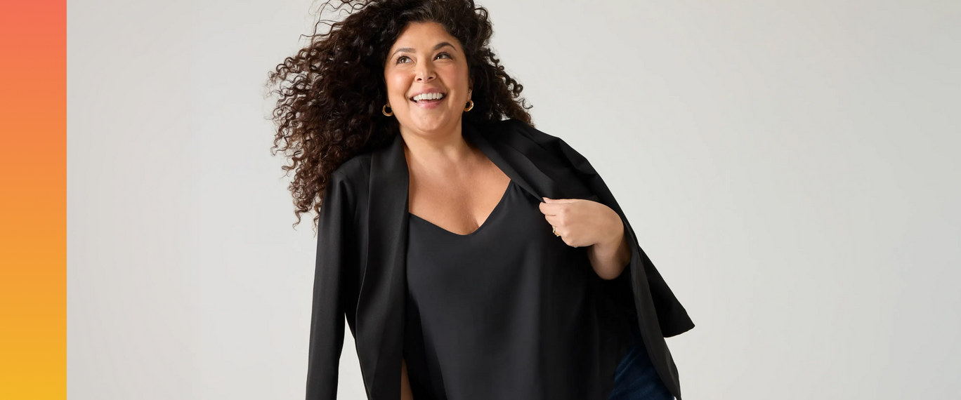 Tiff, Torrid Casting Call 2025 Winner from Los Angeles, California, laughing as the wind blows through her curly hair, wearing a black blazer over a black top.