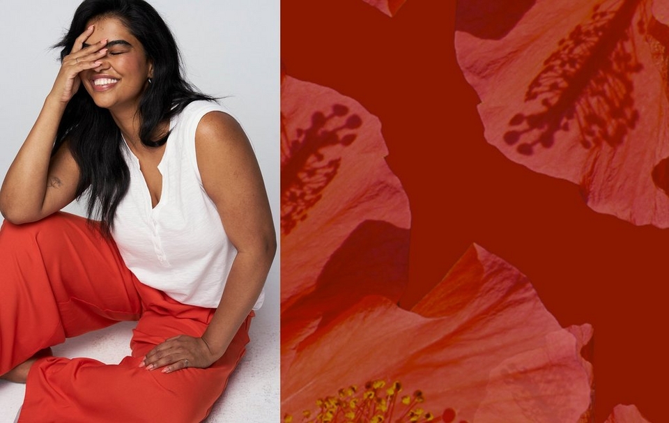 A two-panel image.A two-panel image. On the left, a woman with long dark hair sits on the floor with her knees bent, laughing with her eyes closed and one hand raised to cover her face. She has a small tattoo on her upper arm, wears small stud earrings and a ring, and is dressed in a white sleeveless V-neck top with a button placket and wide-leg red-orange pants. Her nails are painted light pink. The background is a plain light gray. On the right, a close-up macro photo of hibiscus flowers with pink and coral petals, yellow stamens, and a deep red background.