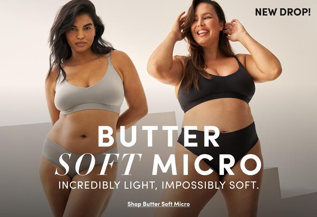 A promotional banner with a warm light gray background showing two women standing together. The woman on the left has long dark hair and wears a light gray seamless wireless bra with a scoop neckline and matching high-waist bikini panties. The woman on the right has long dark wavy hair, smiles with both hands raised to her hair, and wears a black seamless wireless bra with a scoop neckline and matching black high-waist bikini panties. Small black text in the upper right reads 'NEW DROP!' White text overlay reads 'BUTTER SOFT MICRO' in large letters with smaller text reading 'INCREDIBLY LIGHT, IMPOSSIBLY SOFT.' and an underlined link reading 'Shop Butter Soft Micro.'