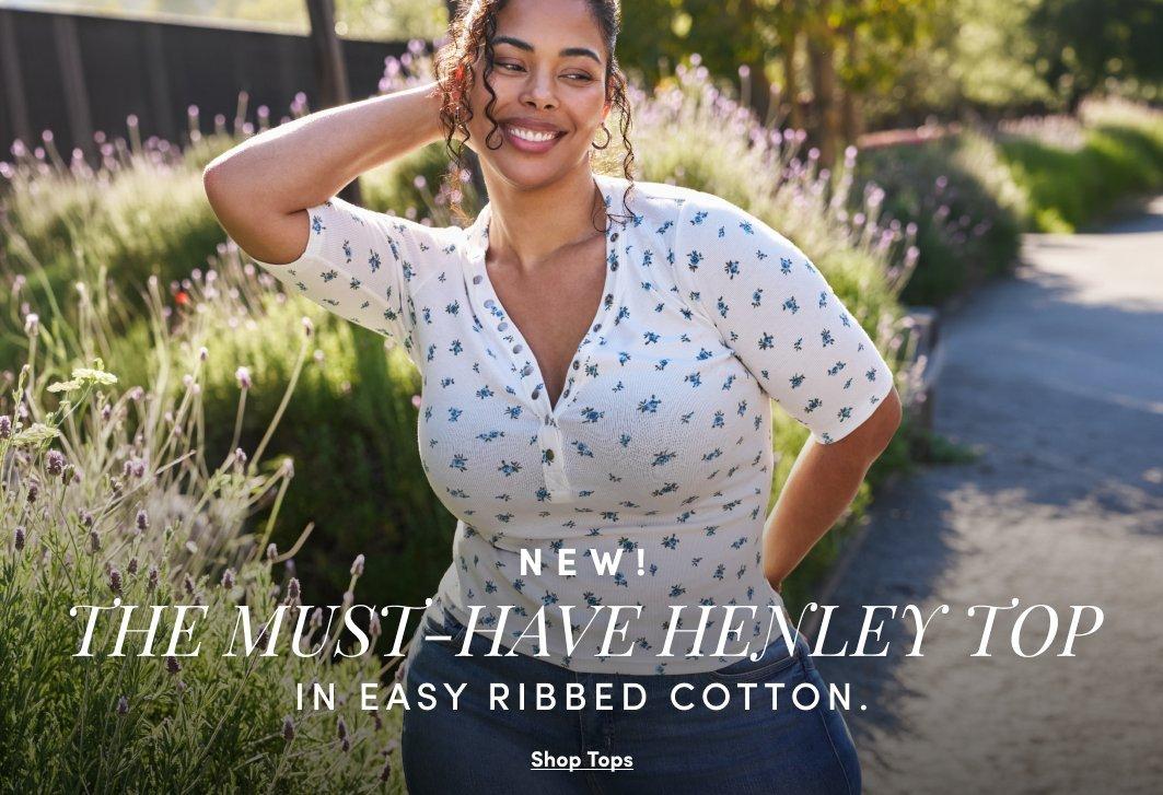 A model smiles outdoors while wearing a white floral ribbed henley top and jeans. Text reads, “New! The Must-Have Henley Top in Easy Ribbed Cotton. Shop Tops.”