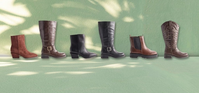 A promotional banner featuring five pairs of summer sandals arranged in a flat lay on a wooden deck and stone surface with tropical succulent foliage in the corner. Styles include tan double-strap buckle slides, white buckle slides, white crochet slides, and black strappy thong sandals.