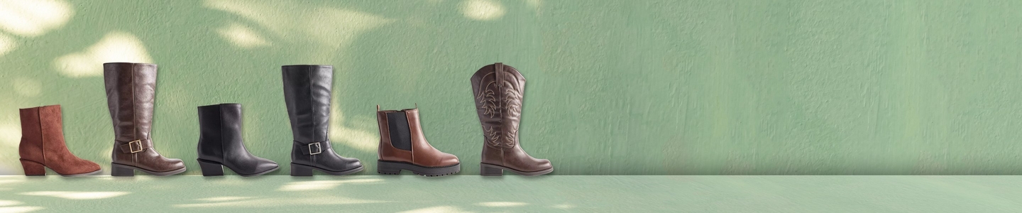 A wide promotional banner featuring five pairs of summer sandals arranged in a flat lay on a wooden deck and stone surface with tropical succulent foliage in the lower right corner. Styles include tan double-strap buckle slides, white buckle slides, white crochet slides, and black strappy thong sandals.