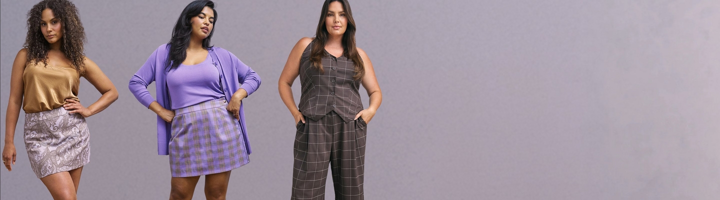 'A wide promotional banner featuring the same plus-size woman with long straight auburn hair shown from two angles against a weathered cream and beige textured wall with a graveled ground. She wears smoky eye makeup, small drop earrings, a fitted black square-neck tank top with a decorative black floral applique detail on one strap, and olive green leggings with an all-over black botanical and peacock jacquard print. On the left she faces slightly forward, and on the right she is seated and angled toward the camera.'