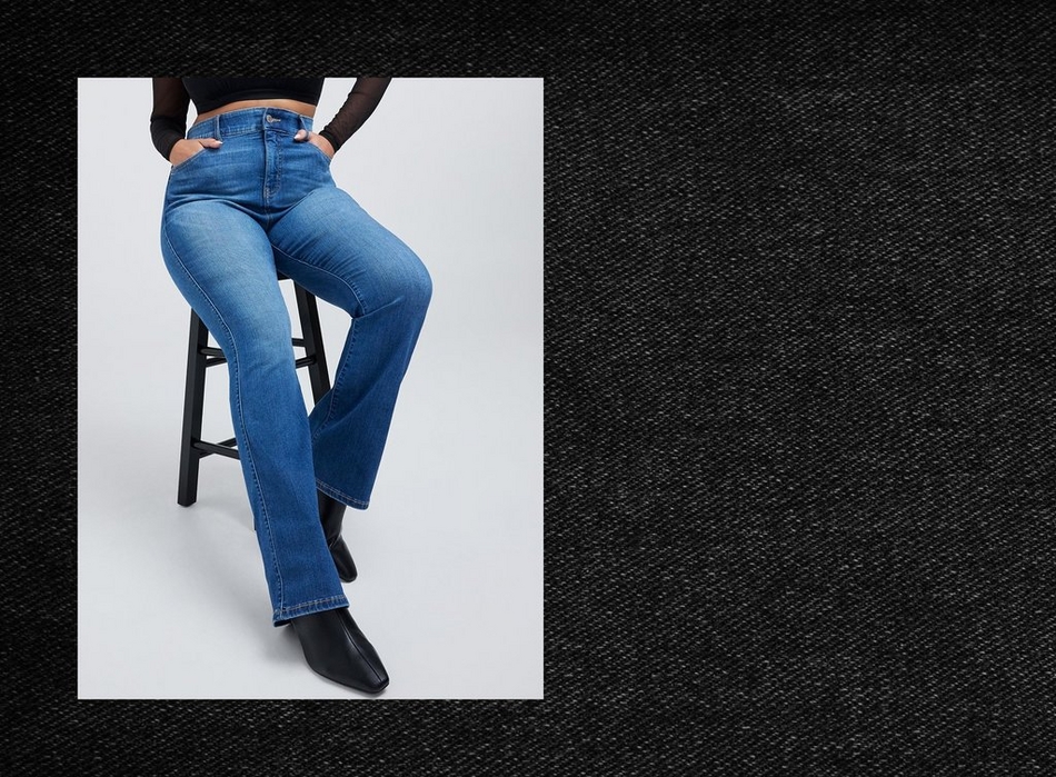 Photo of a woman's lower body seated on a black stool with crossed legs, framed within a rectangular inset against a dark textured charcoal denim-like background. She wears a black long sleeve mesh top cropped above the waist, with both hands tucked into the front pockets of medium wash bootcut jeans featuring a high rise waistband, paired with black pointed toe ankle boots.