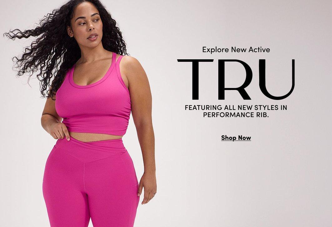 Banner ad for the TRU activewear collection. A woman with curly dark hair stands against a light gray background, wearing a hot pink ribbed tank top and matching leggings with a crossover waistband. Text reads: Explore New Active, TRU, Featuring All New Styles In Performance Rib, Shop Now.