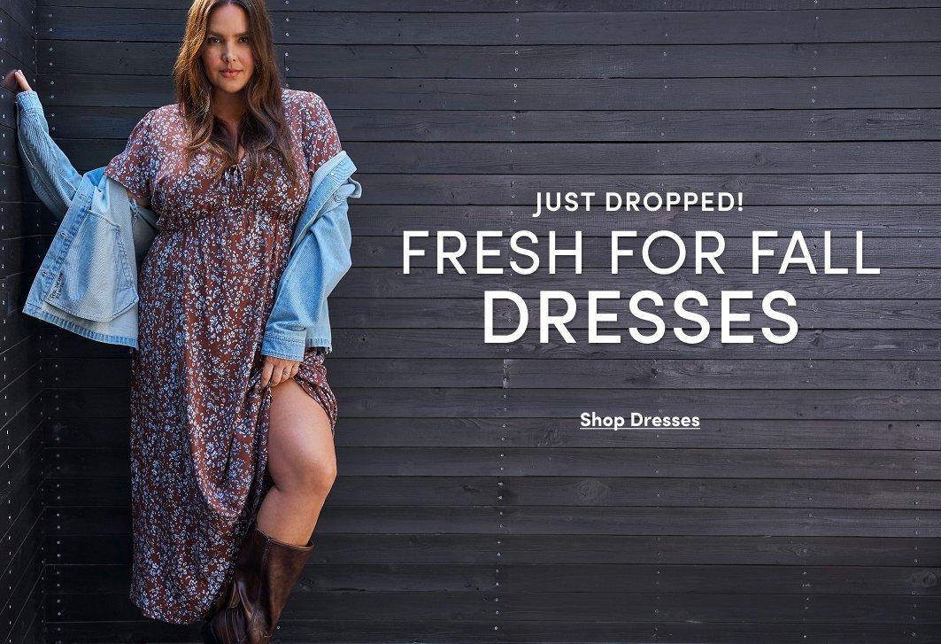 Banner ad for a fall dresses collection. A woman with long brown hair stands against a dark wood-paneled wall, wearing a brown floral maxi dress with a leg slit, a light denim jacket draped off her shoulders, and brown boots. Text reads: Just Dropped! Fresh For Fall Dresses, Shop Dresses.