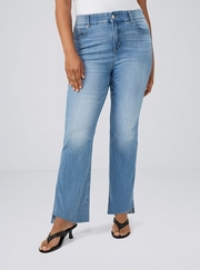 Cropped photo showing a woman's lower body against a plain light gray background, wearing a white top with medium wash bootcut jeans featuring a raw hem, paired with black thong strap heeled sandals, rings visible on her fingers. 