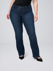 Cropped photo showing a woman's lower body against a plain light gray background, wearing a black top with dark wash bootcut jeans, paired with black suede pointed toe heels. 