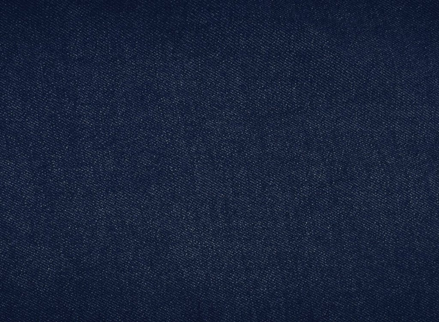 Close-up texture of dark indigo blue denim fabric showing the diagonal twill weave pattern with small white flecks throughout. No people, text, or other elements are present in the image.