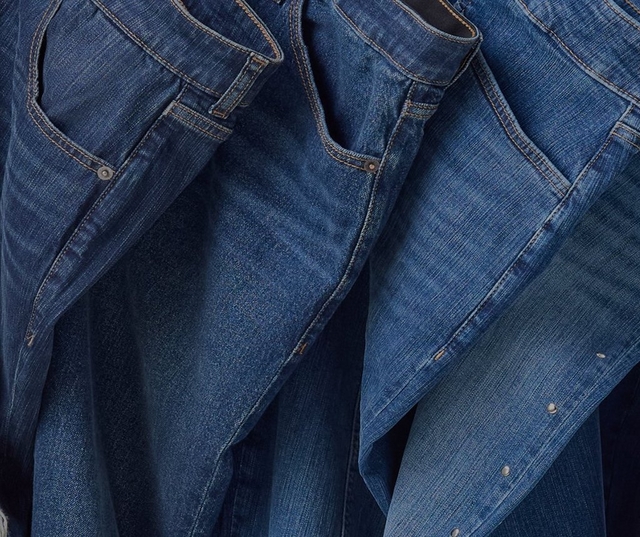 Close-up texture of dark indigo blue denim fabric showing the diagonal twill weave pattern with small white flecks throughout. No people, text, or other elements are present in the image.