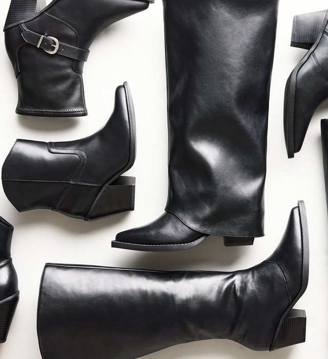 Overhead flat lay of several black faux leather boots and booties arranged closely together, including a knee high boot with a pointed toe, an ankle boot with a buckle strap, and pointed toe booties with block heels. The background is plain white.