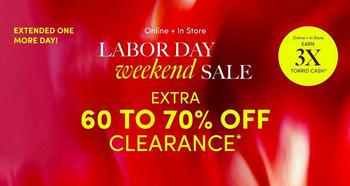 Red and pink gradient background with a floral texture, with white and yellow text overlaid. In the top left corner, a black rectangular banner contains white text reading 'EXTENDED ONE MORE DAY!'. Below it, small white text reads 'Online + In Store'. Underneath, large white text reads 'LABOR DAY' followed by italicized cursive text reading 'weekend' and bold white text reading 'SALE'. In the top right corner, small white text reads 'Deluxe & Diehard Earn' above bold yellow text reading '3X' and smaller white text reading 'TORRID CASH'. Below the headline, bold yellow text reads 'EXTRA' followed by large bold white text reading '60 TO 70% OFF' and yellow text reading 'CLEARANCE' with an asterisk. No people appear in the image.