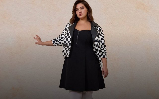 A model wearing a black square-neck fit-and-flare dress layered under a black-and-white checkered moto jacket, with white patterned tights.