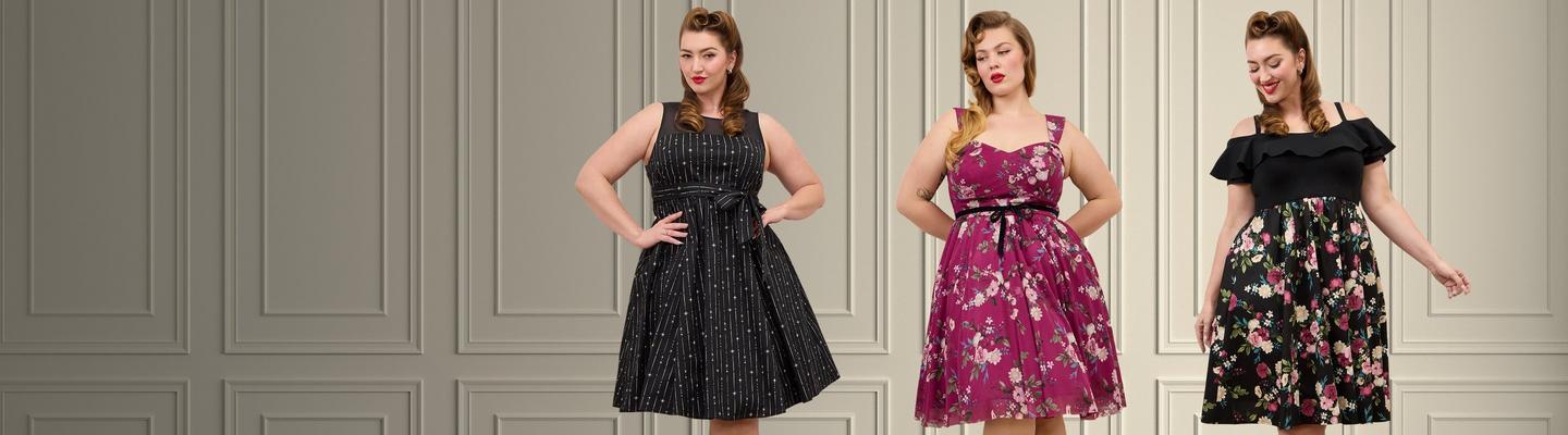 Wide promotional banner featuring two models with pin-up style wavy brown hair and red lipstick against a white paneled wall. Left model wears a red and white gingham fit-and-flare dress with ruffle shoulder straps and a sweetheart neckline. Right model wears a blue fit-and-flare dress with a hot air balloon print, sweetheart neckline, and a full pleated skirt.