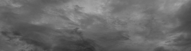 A wide, short banner image of an overcast night sky in deep slate blue. Soft layered clouds drift across the frame, lighter and wispier toward the upper right and darker and denser along the lower left, with a small dense cloud formation near the lower center. There are no people, objects, or text in the image.