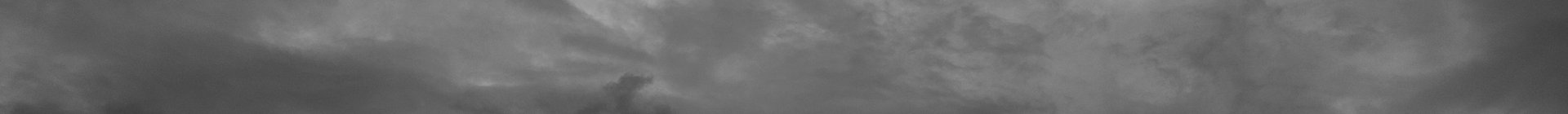 A wide, short banner image of an overcast night sky in deep slate blue. Soft layered clouds drift across the frame, lighter and wispier toward the upper right and darker and denser along the lower left, with a small dense cloud formation near the lower center. There are no people, objects, or text in the image.
